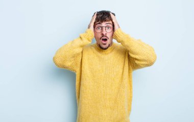 Genç ve yakışıklı bir adam hoş olmayan bir şekilde şok olmuş, korkmuş ya da endişeli görünüyor ağzı sonuna kadar açık ve iki kulağını da elleriyle kapatıyor.