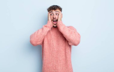 Genç yakışıklı adam mutlu, heyecanlı ve şaşırmış hissediyor, iki eli yüzü yana bakıyor.