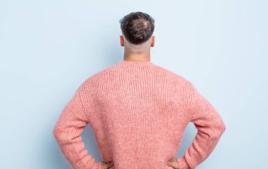 Genç, yakışıklı bir adam kafası karışık ya da dolu ya da şüphe ve soru dolu, merak ediyor, elleri kalçasında, dikiz aynasından.