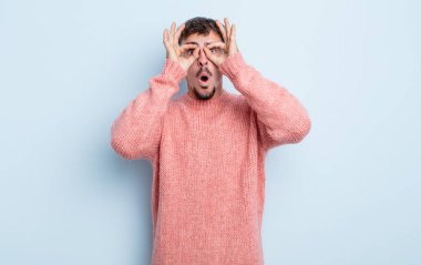 Genç yakışıklı adam şaşkın, şaşırmış ve şaşırmış hissediyor. Elinde şaşkın, inançsız bir bakışla gözlük tutuyor.