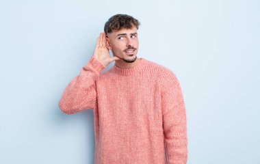 Genç yakışıklı adam ciddi ve meraklı görünüyor, dinliyor, gizli bir konuşma veya dedikodu duymaya çalışıyor, kulak misafiri oluyor.