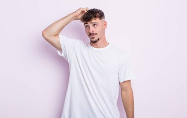 Genç yakışıklı adam şaşkın ve şaşkın hissediyor, başını kaşıyor ve yana bakıyor.