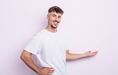 Genç yakışıklı adam kendini mutlu ve neşeli hissediyor, gülümsüyor ve seni selamlıyor, dostça bir jestle içeri davet ediyor.