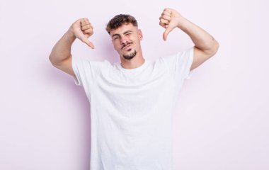 Genç yakışıklı adam üzgün, hayal kırıklığına uğramış ya da kızgın görünüyor, anlaşmazlık içinde baş parmağını gösteriyor, hayal kırıklığına uğramış hissediyor.