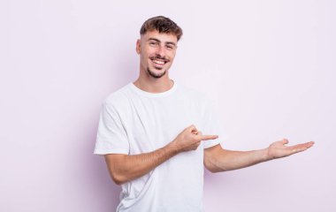 Genç yakışıklı adam gülümsüyor, mutlu, tasasız ve tatmin olmuş hissediyor, fotokopi alanındaki konsepte ya da fikre işaret ediyor.