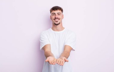 Genç yakışıklı adam mutlu bir şekilde gülümsüyor arkadaş canlısı, kendinden emin, olumlu bakışlı, bir nesne ya da konsept sunuyor ve gösteriyor.