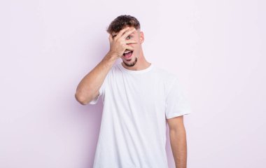 Genç yakışıklı adam şok olmuş, korkmuş ya da korkmuş görünüyor. Yüzü elle kaplanmış ve parmaklarının arasından gizlice bakıyor.
