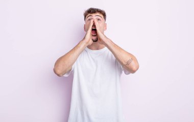 Genç yakışıklı adam mutlu, heyecanlı ve pozitif hissediyor. Elleri ağızda, bağırıyor.