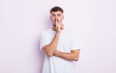 Genç ve yakışıklı adam ciddi görünüyor ve parmaklarını dudaklarına bastırıp sessizlik ya da sessizlik talep ediyor, sır saklıyor.