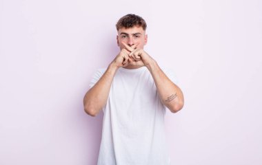 Genç ve yakışıklı bir adam ciddi ve hoşnutsuz görünüyor. İki parmağın önde olsun, reddedilsin ve sessizlik istesin.