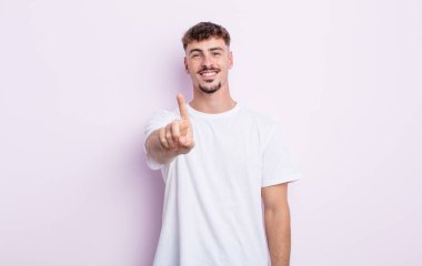 Genç ve yakışıklı bir adam gururla gülümsüyor ve gururla bir numaralı pozu veriyor, kendini lider gibi hissediyor.