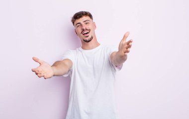 Genç yakışıklı adam neşeyle gülümsüyor sıcak, dostça, sevgi dolu bir kucak veriyor, mutlu ve sevimli hissediyor.