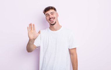 Genç yakışıklı adam mutlu ve neşeyle gülümsüyor, el sallıyor, seni selamlıyor ve selamlıyor, ya da hoşça kal diyor.