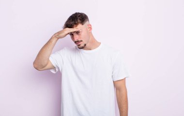 Genç yakışıklı adam şaşkın ve şaşkın bakıyor, el üstünde uzak bakıyor, izliyor ya da arıyor