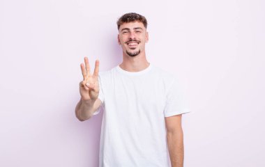 Genç yakışıklı adam gülümsüyor ve arkadaş canlısı görünüyor, üç ya da üç numarayı gösteriyor, eli önde, geriye doğru sayıyor.