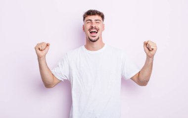 Genç yakışıklı adam çok mutlu ve şaşırmış görünüyor, başarıyı kutluyor, bağırıyor ve zıplıyor.