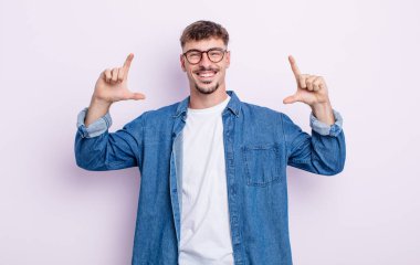 Genç yakışıklı bir adam kendi gülüşünü çiziyor ya da özetliyor iki eliyle, pozitif ve mutlu görünüyor, sağIık kavramı.