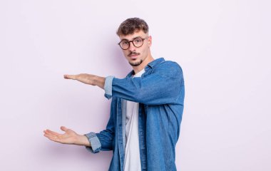 Genç yakışıklı bir adam iki eli de yan tarafında fotokopi alanı olan bir nesneyi tutuyor, bir nesneyi gösteriyor, sunuyor ya da reklamını yapıyor.