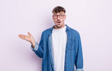 Genç yakışıklı adam şaşırmış ve şoka uğramış görünüyor, çenesi düşmüş, eli açık bir nesneyi tutuyor.