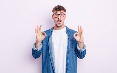 Genç yakışıklı adam şok olmuş, şaşırmış ve şaşırmış hissediyor. Onaylıyor. İki eliyle de onay işareti yapıyor.