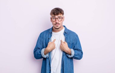 Genç ve yakışıklı bir adam kendini işaret ediyor. Şaşırmış ve şaşırmış bir şekilde bakıyor.