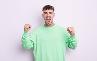 Genç yakışıklı bir adam sinirli bir ifadeyle ya da yumruklarıyla başarıyı kutlarken agresif bir şekilde bağırıyor.