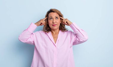 Orta yaşlı bir kadın kafası karışık ya da şüpheci, bir fikre odaklanmış, çok düşünüyor, kenarda boşluklar arıyor.