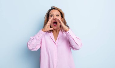 Orta yaşlı kadın mutlu, heyecanlı ve pozitif hissediyor. Elleri ağızda, bağırarak bağırıyor.