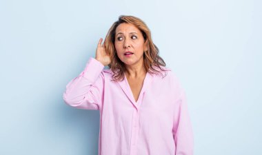 Orta yaşlı kadın gülümsüyor, tuhaf bir şekilde yan tarafa bakıyor, dedikoduları dinlemeye ya da bir sırrı duymaya çalışıyor.