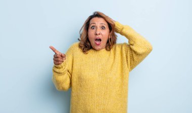 Orta yaşlı bir kadın gülüyor, mutlu, pozitif ve şaşırmış görünüyor, yanal fotokopi alanını işaret eden harika bir fikrin farkına varıyor.