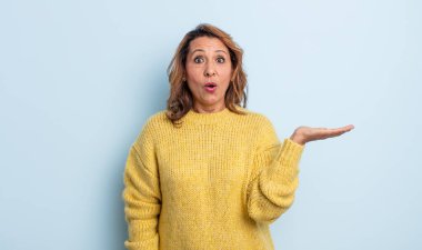 Orta yaşlı kadın şaşırmış ve şoka uğramış görünüyor, çenesi düşmüş ve eli açık bir nesneyi tutuyor.