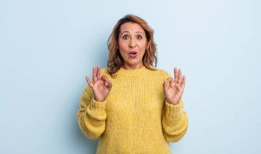 Orta yaşlı kadın şok olmuş, şaşırmış ve şaşırmış hissediyor. Onaylıyor. İki eliyle de onay işareti yapıyor.