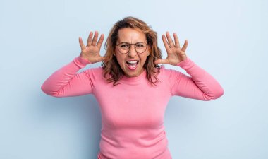 Panik içinde bağıran orta yaşlı bir kadın, şok olmuş, korkmuş ya da öfkeli, elleri başının yanında.