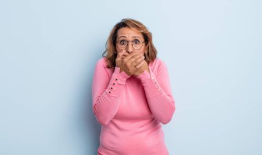 Orta yaşlı bir kadın şok olmuş, şaşırmış bir ifadeyle ağzını kapatıyor, sır saklıyor ya da 