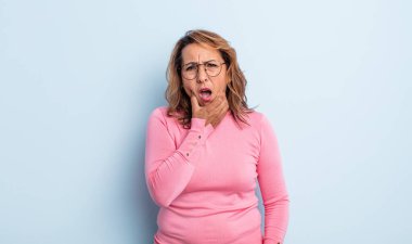 Orta yaşlı, ağzı ve gözleri açık ve eli çenesinde olan bir kadın. Hoş olmayan bir şok geçiriyor. Ne diyor?