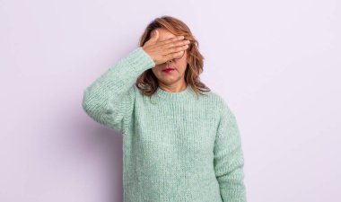 Orta yaşlı bir kadın tek eliyle gözlerini kapatıyor korkmuş ya da endişeli hissediyor, merak ediyor ya da körü körüne bir sürpriz bekliyor.