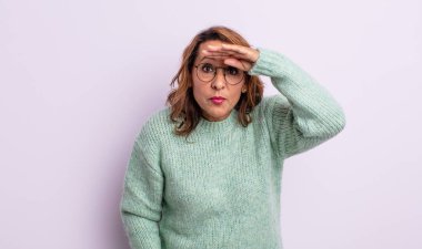 Orta yaşlı kadın şaşkınlık ve şaşkınlık içinde bakıyor. Alnı açık, uzaklara bakıyor, izliyor ya da arıyor.