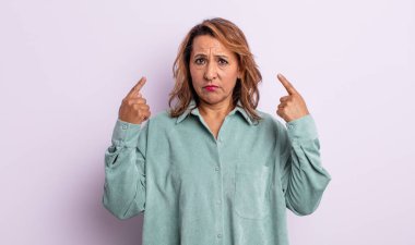 Kötü tavırlı orta yaşlı bir kadın gururlu ve agresif görünüyor, yukarıyı gösteriyor ya da elleriyle alay işareti yapıyor.