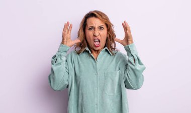 Orta yaşlı bir kadın elleri havada bağırıyor. Öfkeli, sinirli, stresli ve üzgün.