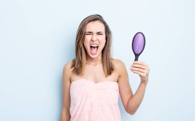 Genç ve güzel bir kadın agresif bir şekilde bağırıyor, çok kızgın görünüyor. saç fırçası konsepti