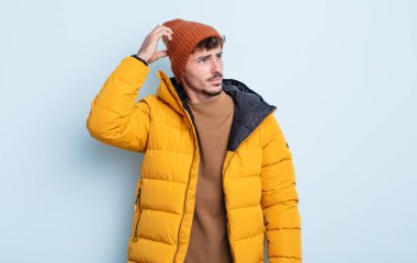 Kafası karışmış, kafası karışmış, kaşınan genç, yakışıklı bir adam. kış konsepti