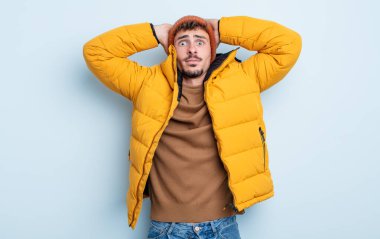 Genç ve yakışıklı bir adam stresli, endişeli ya da korkmuş hissediyor. Elleri başının üstünde. kış konsepti