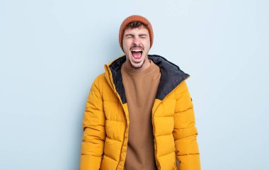 Genç yakışıklı adam agresif bir şekilde bağırıyor, çok kızgın görünüyor. kış konsepti