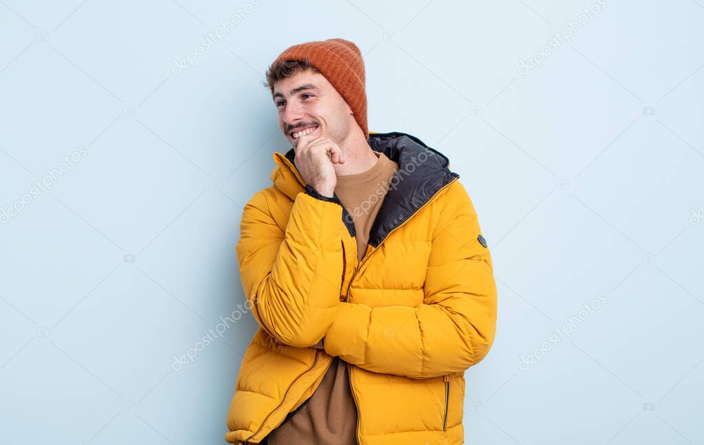 young handsome man smiling with a happy, confident expression with hand on chin. winter concept