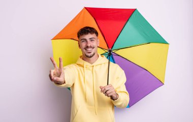 Genç yakışıklı adam gülümsüyor ve mutlu görünüyor, zafer ya da barış işareti yapıyor. şemsiye kavramı