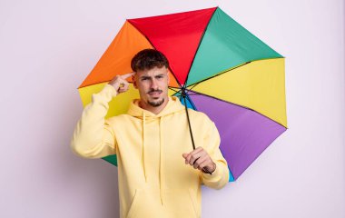 Genç yakışıklı adam kafası karışık ve şaşkın hissediyor, deli olduğunu gösteriyor. şemsiye kavramı