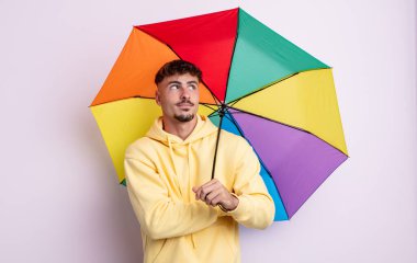 Genç yakışıklı adam omuz silkiyor, kafası karışık ve kararsız. şemsiye kavramı