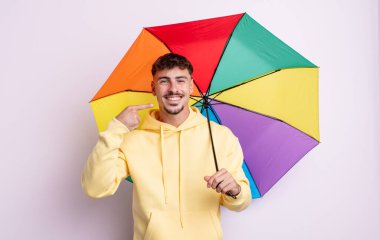 Genç ve yakışıklı bir adam kendi gülüşünü işaret ederek kendine güvenerek gülümsüyor. şemsiye kavramı