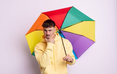Ağzı ve gözleri açık ve eli çenesinde genç yakışıklı bir adam. şemsiye kavramı