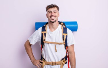 Genç yakışıklı adam mutlu bir şekilde gülümsüyor, eli kalçasında ve kendinden emin. Yürüyüş konsepti